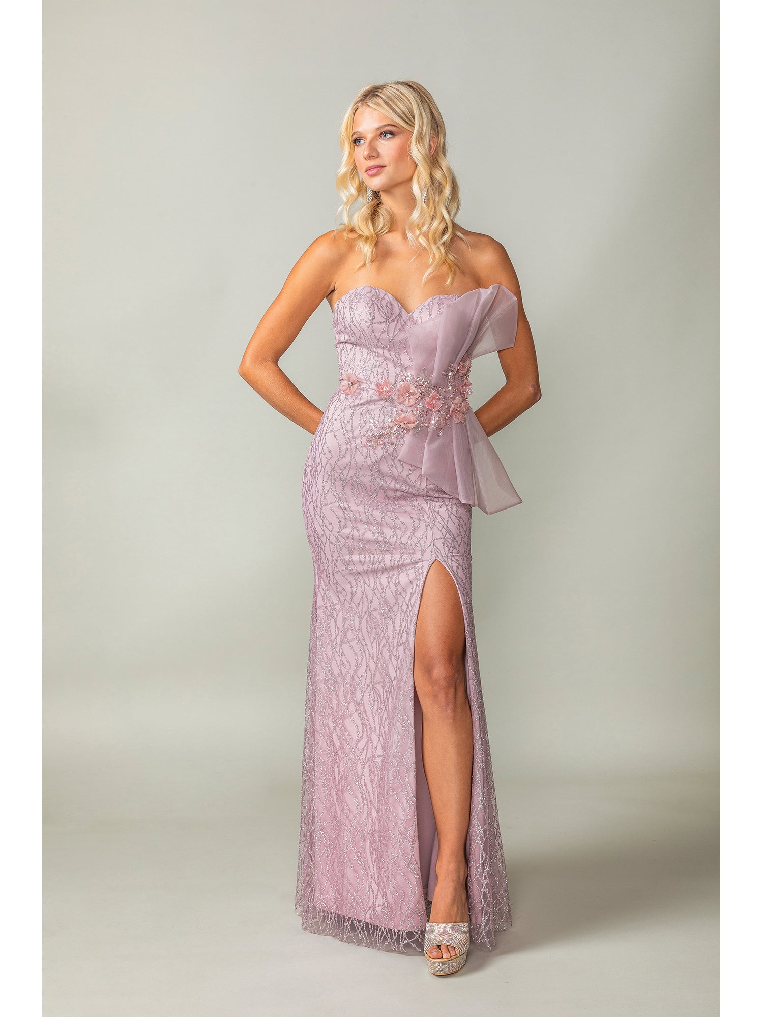 A woman models the Side-Bow Strapless Long Glitter Prom Dress 4394, a strapless, floor-length light pink gown with a thigh-high slit and sparkling floral accents, posing against a plain background.